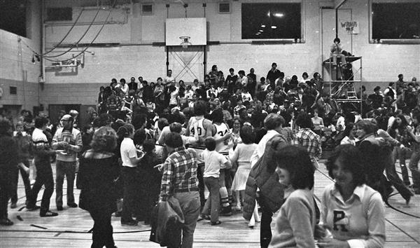 Crowd of students in a gymnasium with a scaffold visible in the background where a broadcaster was set up.